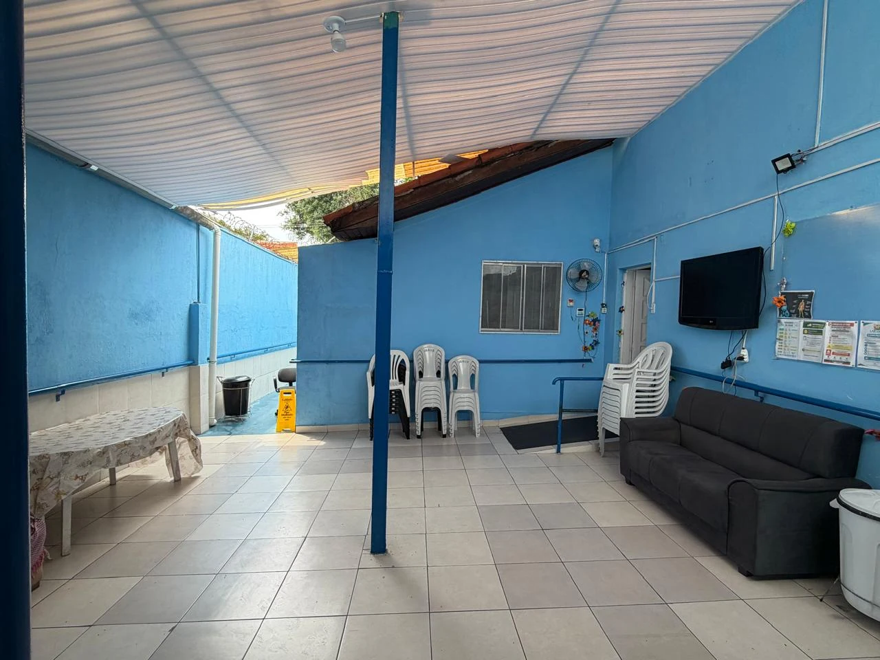 Espaço de convivência na varanda com sofá, cadeiras e televisão